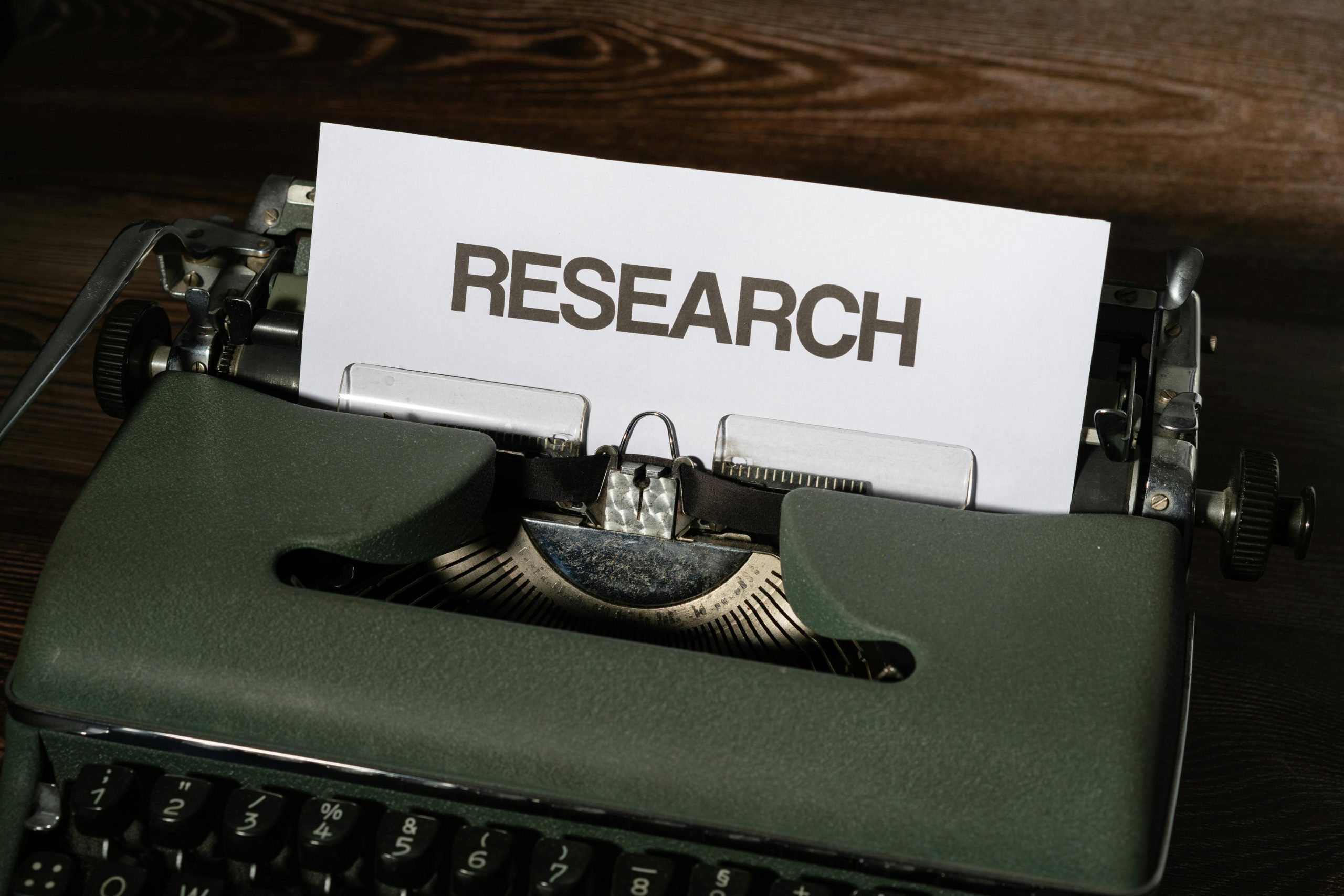 Close-up of a vintage typewriter with a paper labeled 'Research' inserted, on a wooden surface.